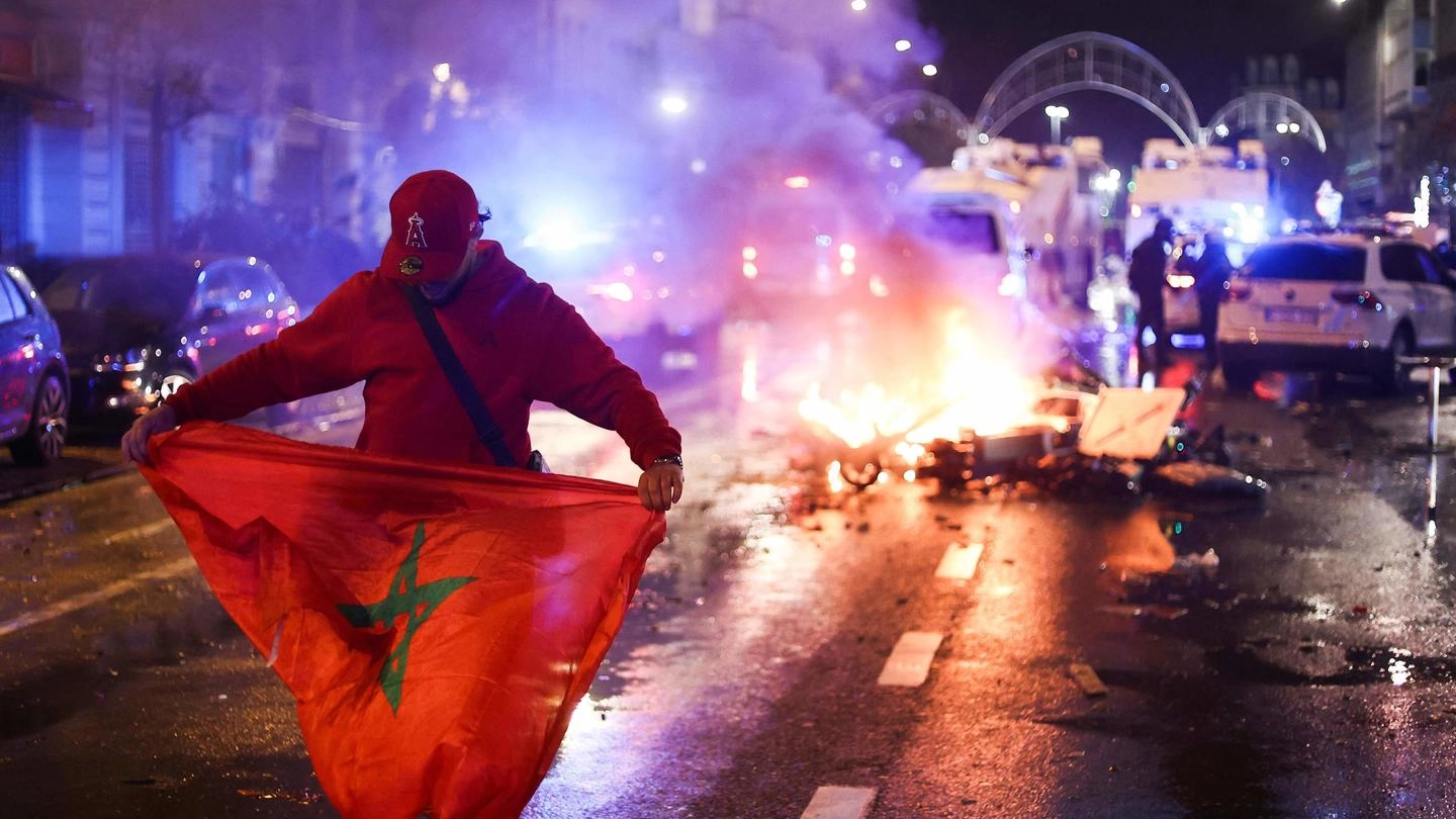 Un tifoso regge una bandiera del Marocco, sullo sfondo gli scontri (Afp)