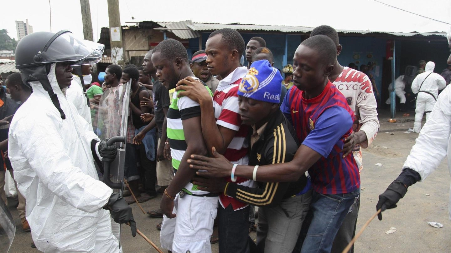 Ebola, la polizia controlla alcuni abitanti in attesa della distribuzione del cibo in Liberia (Ansa)