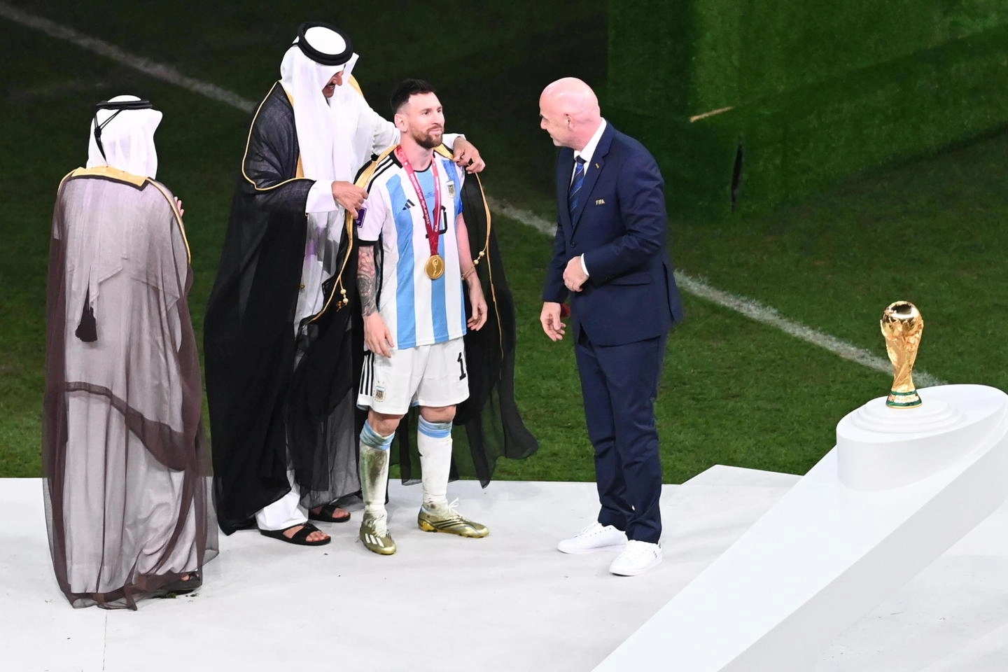 Messi riceve il mantello dall'emiro del Qatar sotto gli occhi di Infantino (Ansa)
