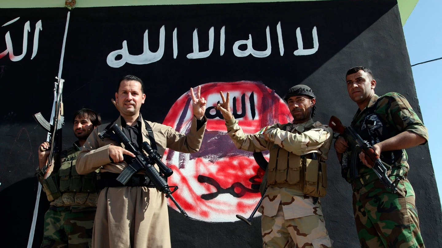I peshmerga davanti alla bandiera dell'Isis disgnata su un muro a Zumar (Reuters)