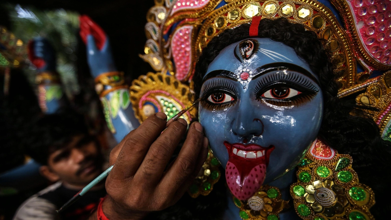 Un artista indiano dipinge il volto della dea Kalì (Ansa)