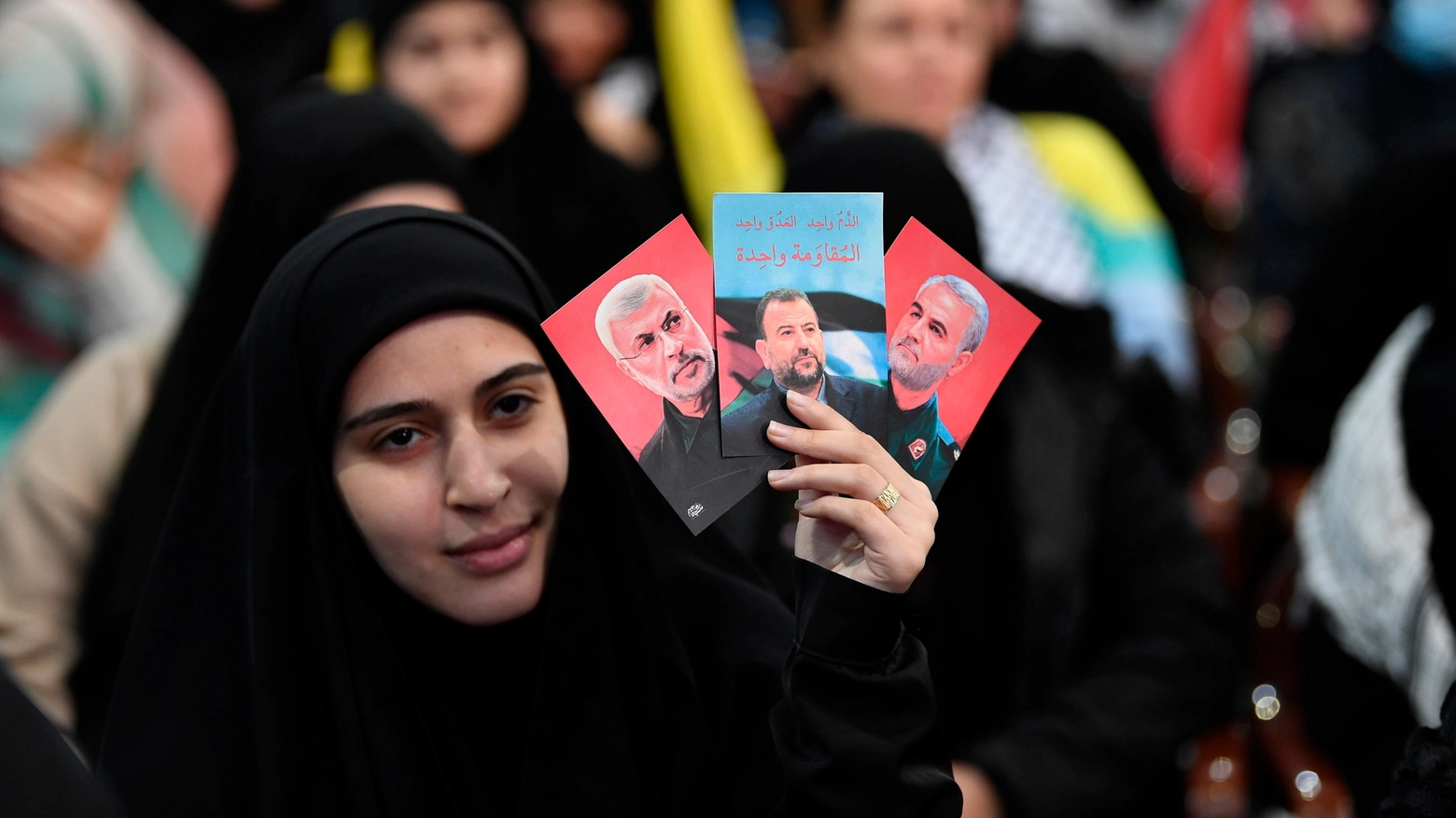 Una donna tiene in mano i ritratti di Abu Mahdi al-Muhandis, di Saleh al-Arouri e di Qasem Soleimani (Ansa)