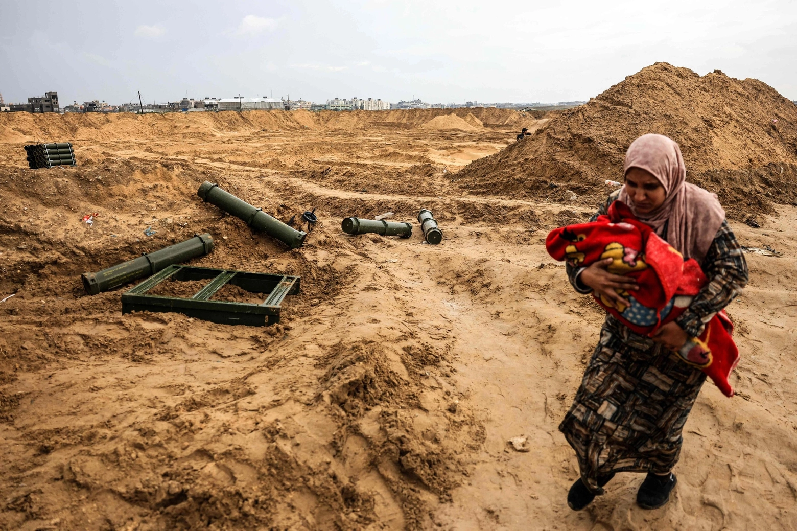 Khan Yunis, una donna palestinese con il figlio passa a fianco a contenitori di munizioni lasciati dai militari israeliani