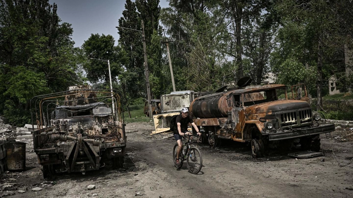 Un uomo in bici tra mezzi militari distrutti a Lysychansk, nel Donbass (Ansa)