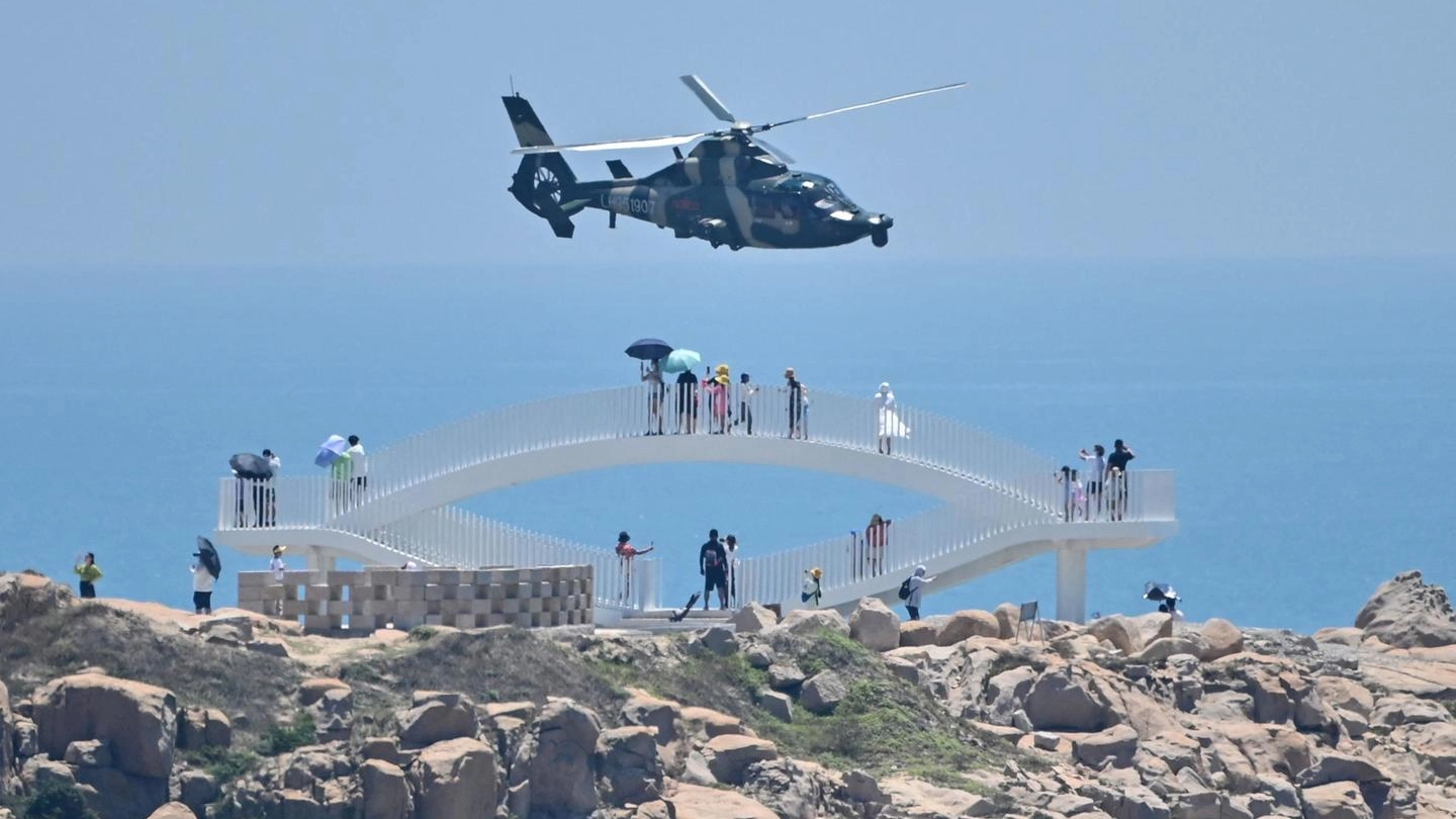Turisti guardano un elicottero militare cinese che sorvola l'isola di Pingtan (Ansa)