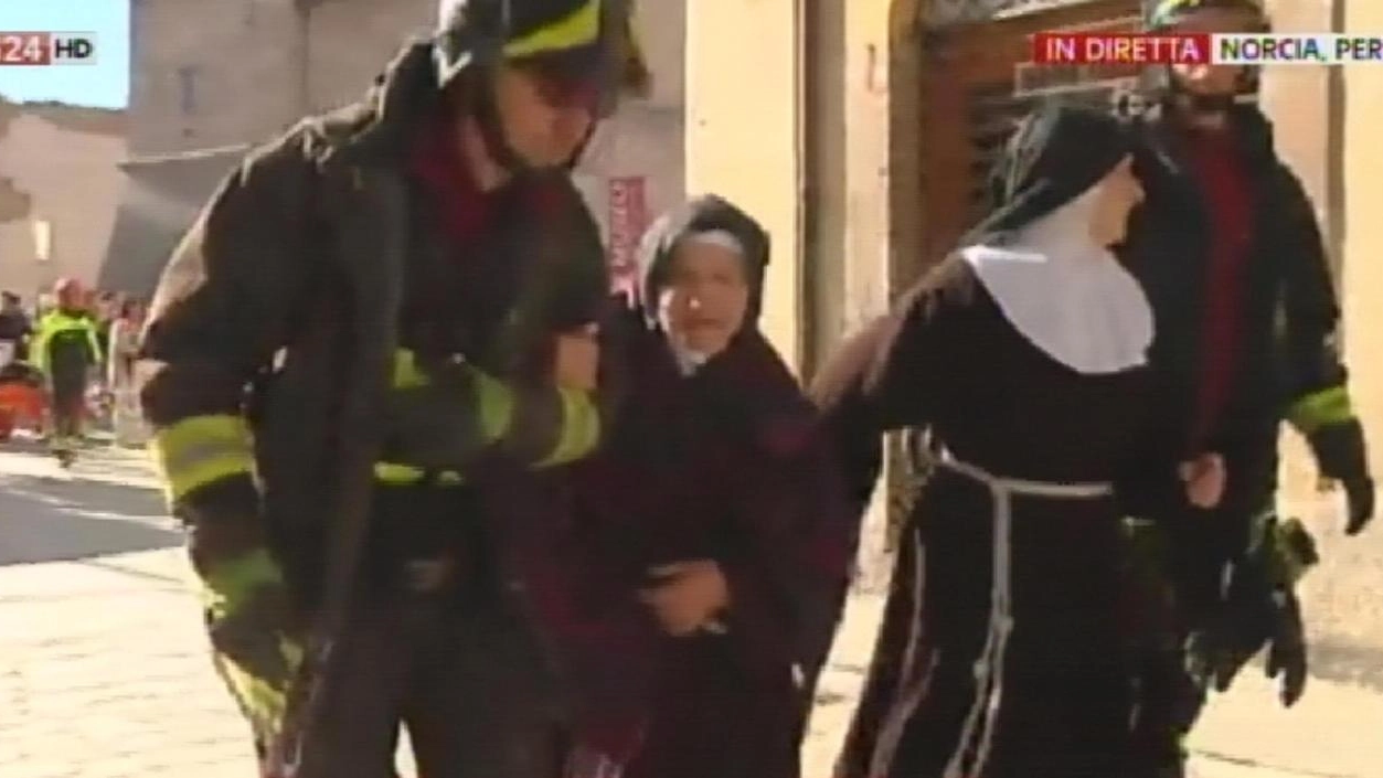 Vigili del fuoco assistono alcune suore dopo il crollo della basilica a Norcia (Ansa)