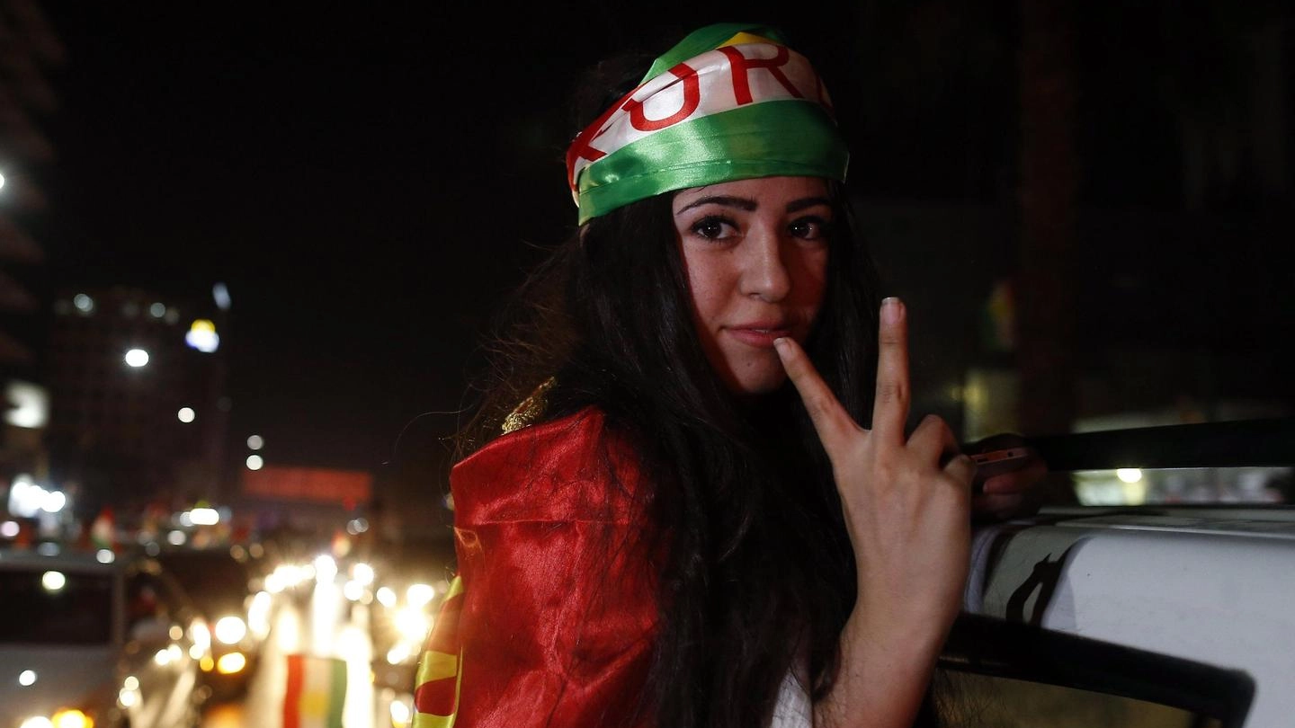 Una giovane curda festeggia in strada avvolta nei suoi colori