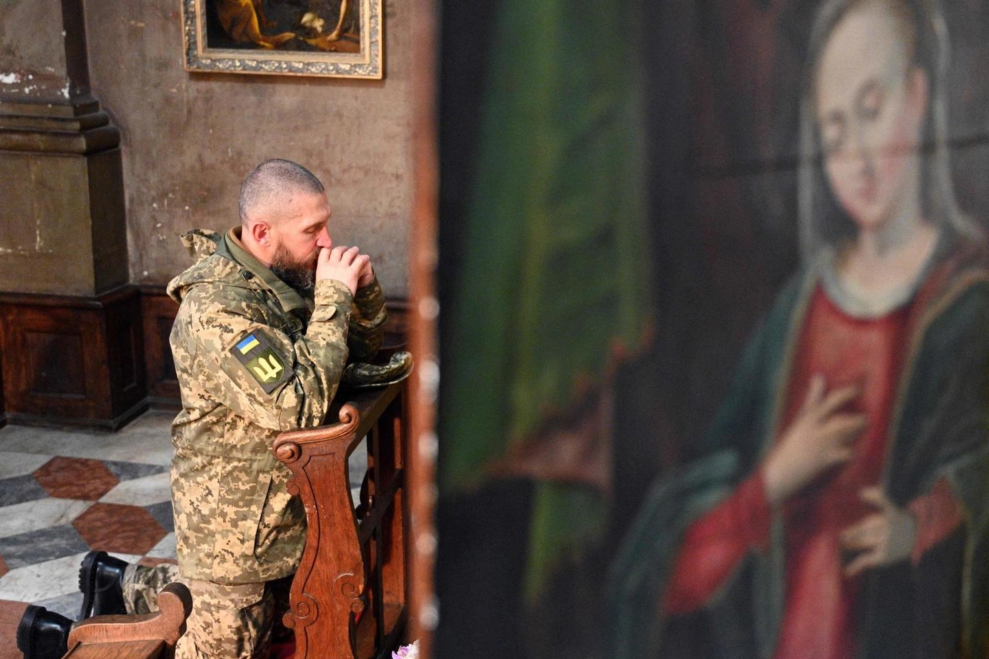 La preghiera di un soldato ucraino durante il funerale di un compagno (Ansa)