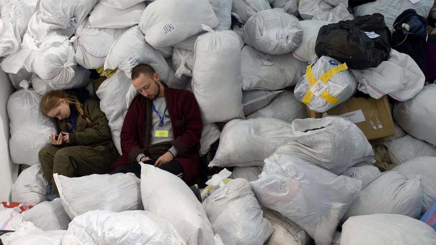 Volontari si riposano sopra i sacchi di vestiti per i rifugiati (Ansa)