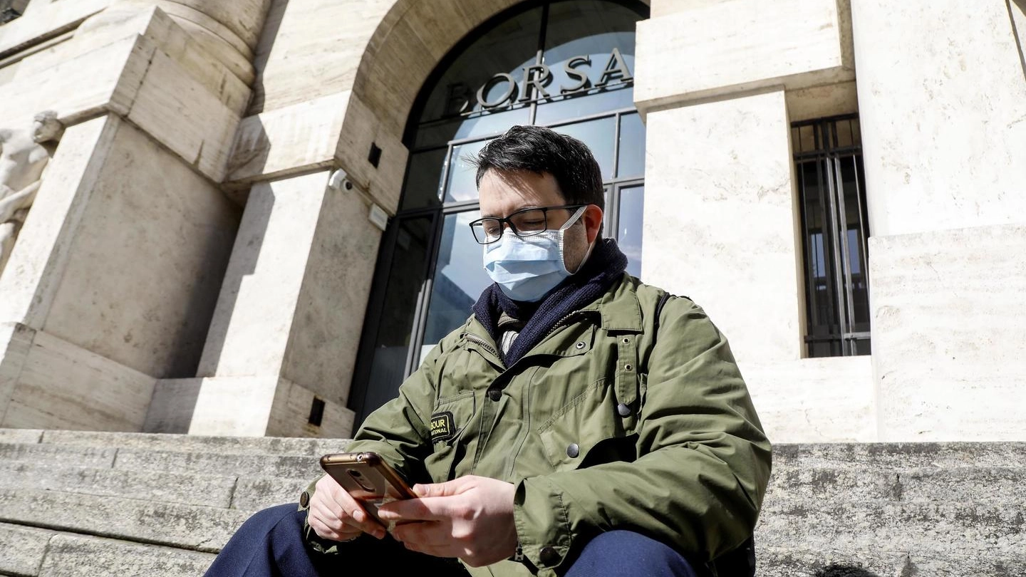 Persone con mascherine per proteggersi dal Coronavirus a Piazza Affari (Ansa)