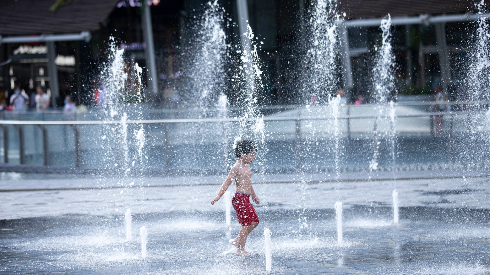 Un bambino si rinfresca nelle fontane di piazza Gae Aulenti a Milano (Ansa)