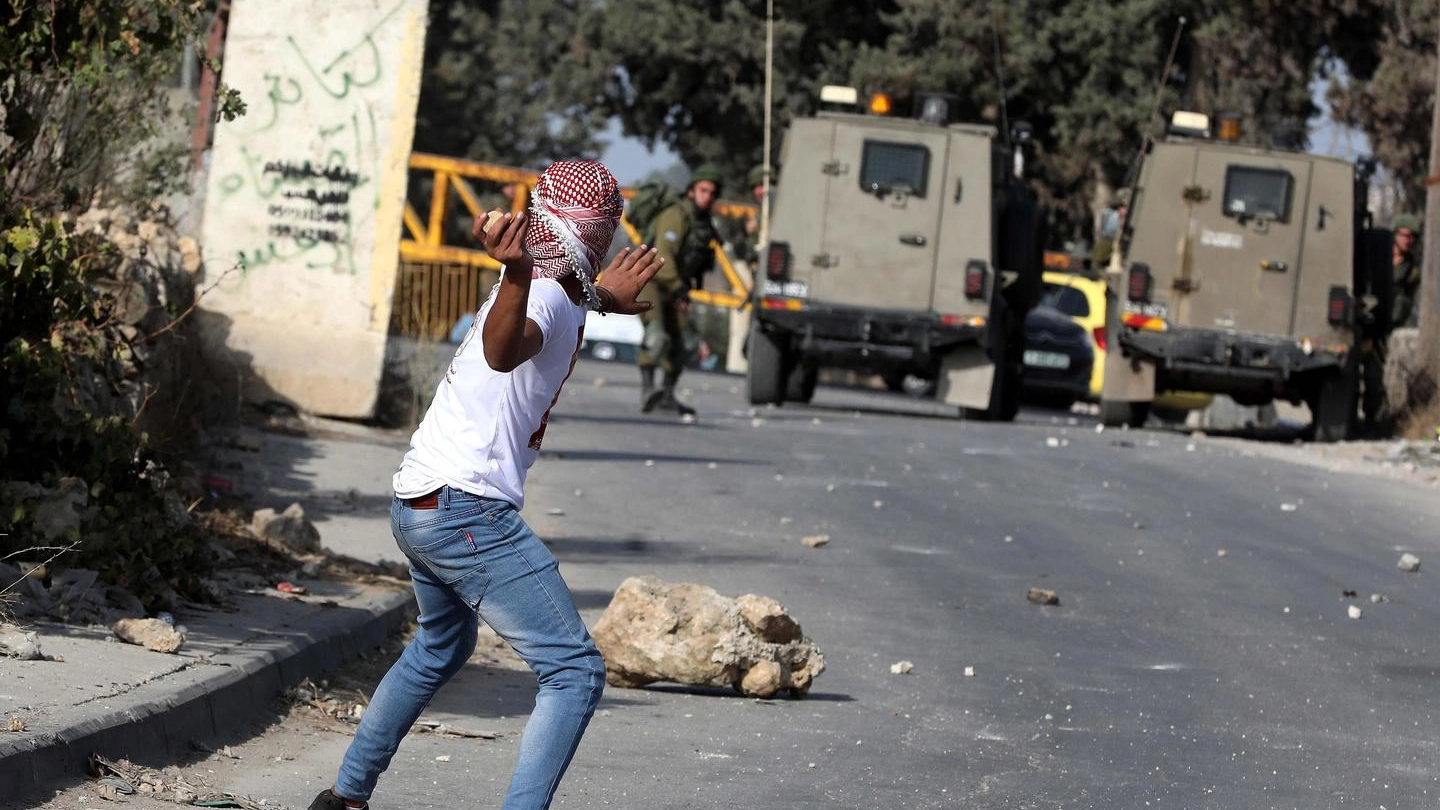 Un palestinese lancia un sasso contro i militari israeliani a Hebron (Ansa)