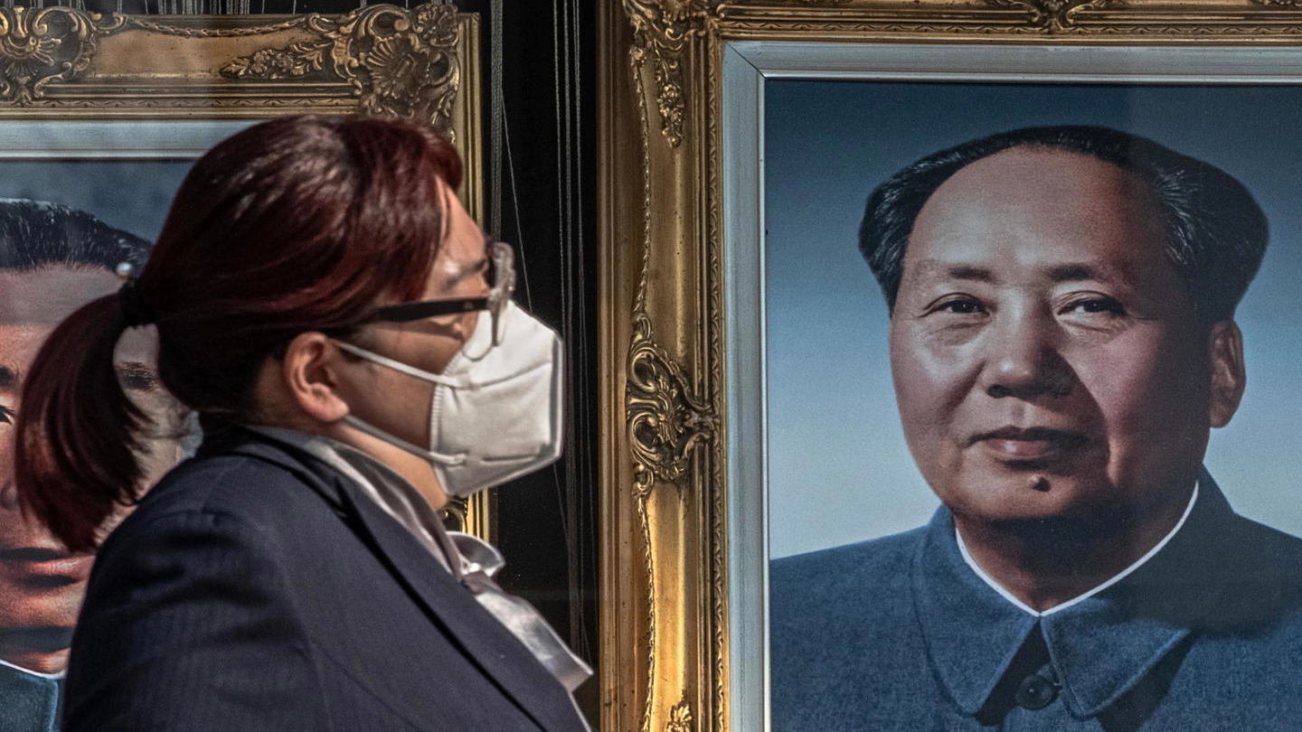 Una donna si protegge dal contagio; dietro il ritratto di Mao (Ansa)