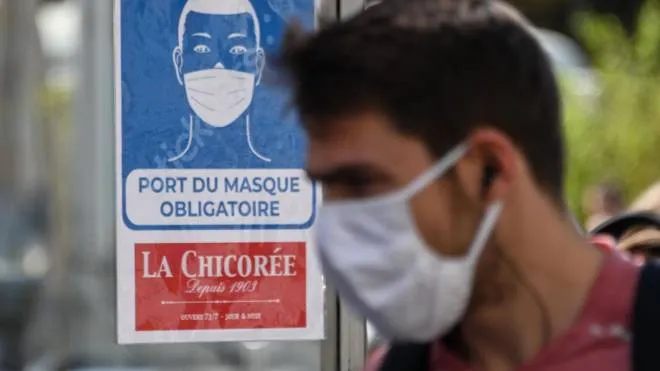 A man wearing a protective face mask due to the COVID-19 coronavirus pandemic, walks past a mandatory wearing mask sign in front of a shop in a pedestrian street in Lille on July 20, 2020, as masks become mandatory in all indoor public spaces. (Photo by DENIS CHARLET / AFP)