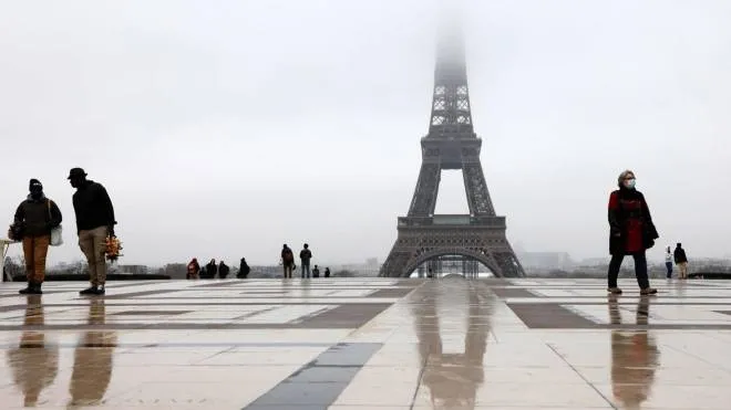 People with face masks walk on the Trocadero plaza on January 27, 2021 in Paris in front of the Eiffel tower whose top disappears in the fog. (Photo by Ludovic MARIN / AFP)