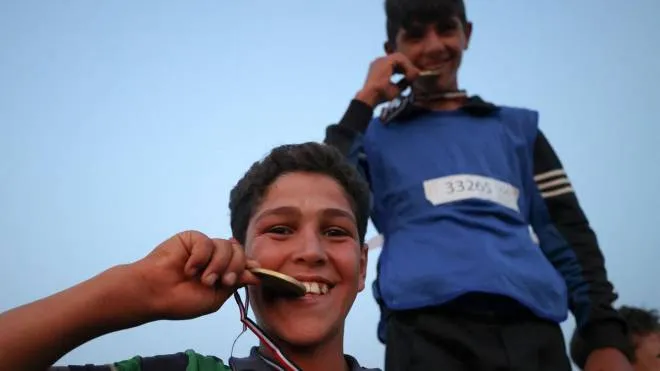 Displaced Syrian boys celebrate their victory by biting their medals won during the so-called "Camp Olympics 2020" in the town of Fuaa, in the northwestern Syrian last major rebel bastion of Idlib, on August 7, 2021, as 120 boys from 12 different camps for displaced people gather for their own version of the Olympic games, at the end of the Tokyo Olympics. - The Idlib region is home to nearly three million people, two-thirds of them displaced from other parts of the country during the ten-year-old conflict. The majority of those who have lost their homes live in camps dotted across the jihadist-dominated region, depending on humanitarian aid to survive and battling cold and floods in winter. (Photo by OMAR HAJ KADOUR / AFP)