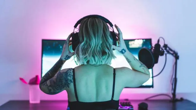 A female gamer and streamer is playing video games on her computer. She is putting on her headphones, getting ready to play and livestream.