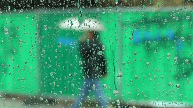 epa09642965 A man holds an umbrella while walking during heavy rain in Nicosia, Cyprus, 15 December 2021.  EPA/KATIA CHRISTODOULOU SEEN THROUGH GLASS
