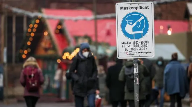 epa09653932 Visitors walk behind a sign indicating that face masks are mandatory at the Christmas market in Bremen, northern Germany, 22 December 2021. In order to curb the spread of the Omicron mutation of the Coronavirus, Germany is tightening protective measures after the Christmas holidays.  EPA/FOCKE STRANGMANN