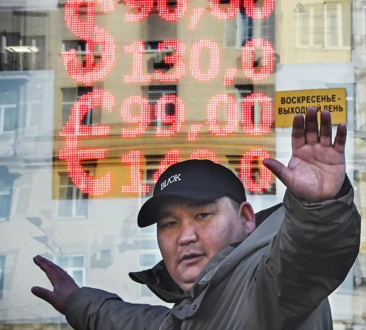 Un cittadino moscovita di fronte a una filiale del cambio, con un cartellone con le quotazioni del rublo in picchiata