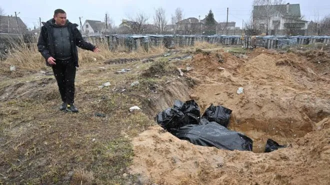TOPSHOT - A man gestures at a mass grave in the town of Bucha, northwest of the Ukrainian capital Kyiv on April 3, 2022. - Ukraine and Western nations accused Russian troops of war crimes after the discovery of mass graves and "executed" civilians near Kyiv, prompting vows of action at the International Criminal Court. City mayor Anatoly Fedoruk told AFP that 280 other bodies had been buried in mass graves. One rescue official said 57 people were found in one hastily dug trench behind a church. (Photo by Sergei SUPINSKY / AFP)