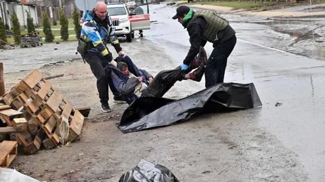 EDITORS NOTE: Graphic content / Communal workers carry the body of a man into a body bag after he was killed in Russian army shelling of the town of Bucha, not far from the Ukrainian capital of Kyiv on April 3, 2022. (Photo by Sergei SUPINSKY / AFP)