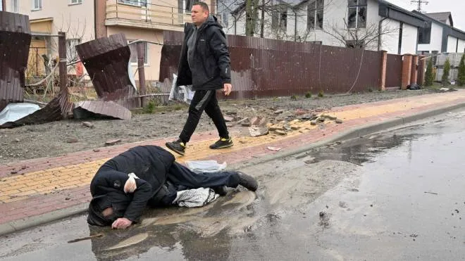EDITORS NOTE: Graphic content / CAPTION ADDITION - A man walks past a body of civilian in the town of Bucha, not far from the Ukrainian capital of Kyiv on April 3, 2022. Britain, France, Germany, the US and NATO all voiced horror at Ukrainian reports on April 2, 2022, of nearly 300 bodies lying in the street in Bucha, with some appearing to have been bound by their hands and feet before being shot. - The Kremlin on April 4, 2022 rejected accusations that Russian forces were responsible for killing civilians near Kyiv. "We categorically reject all allegations," Kremlin spokesman Dmitry Peskov told journalists. (Photo by Sergei SUPINSKY / AFP)
