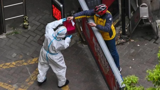 A worker wearing protective gear (L) receives an item from a delivery worker at the entrance of a compound during the second stage of a pandemic lockdown in Jing' an district in Shanghai on April 5, 2022. (Photo by Hector RETAMAL / AFP)