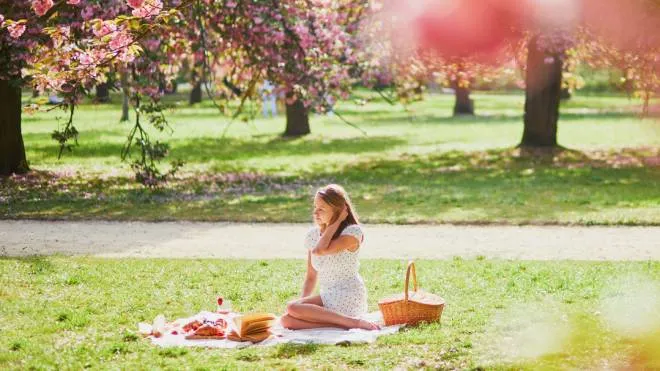 Beautiful young woman having picnic on sunny spring day in park during cherry blossom season