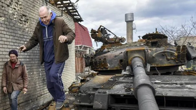 Civili ucraini esplorano un tank russo distrutto nella cittadina di Hostomel, nei sobborghi della capitale ucraina