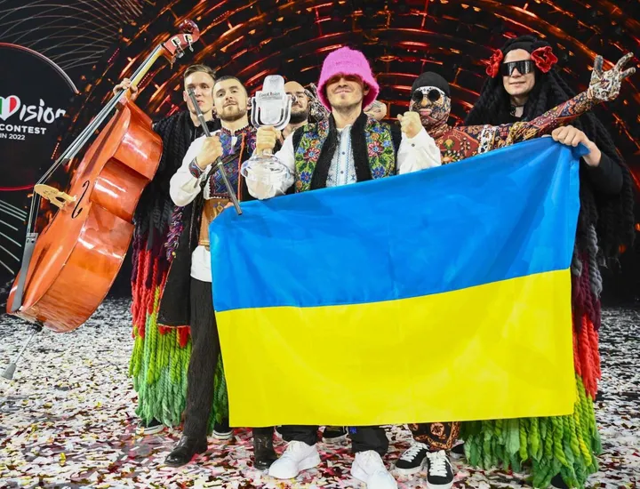 Il gruppo Kalush Orchestra festeggia la vittoria all’Eurovision 2022 dietro una bandiera dell’Ucraina
