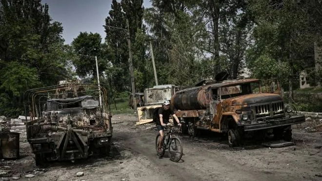 TOPSHOT - A man rides his bicycle between two destroyed military trucks in the city of Lysychansk, eastern Ukrainian region of Donbas, on June 11, 2022. (Photo by ARIS MESSINIS / AFP)