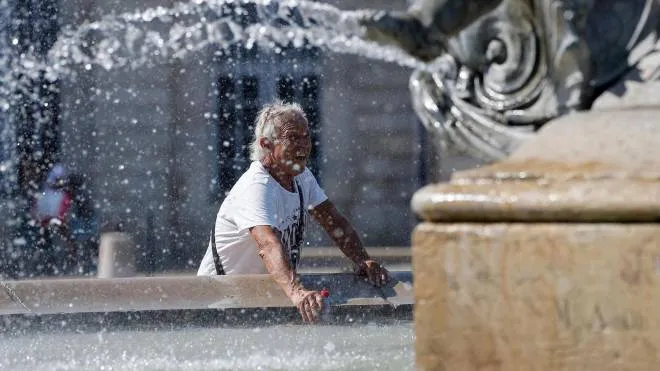 A man puts his bottle in the water of a fountain to cool it down during a heatwave, on July 18, 2022 in Bordeaux. - Fifteen departments, mostly on the western side of France, are placed under "red vigilance" as a heat wave hits the country and should reach its peak on July 18, 2022. (Photo by ROMAIN PERROCHEAU / AFP)