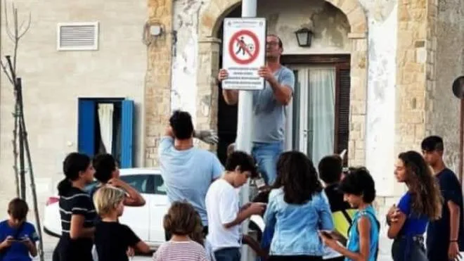 I bambini di Roca di Melendugno, in provincia di Lecce, assistono all’installazione del cartello nella piazza, con il quale si vieta di giocare a pallone