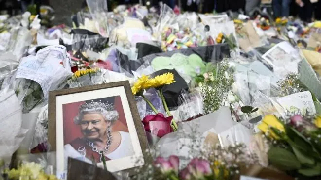 TOPSHOT - A picture of Britain's Queen Elizabeth II is seen amongst flowers put down by well-wishers outside of Buckingham Palace in London on September 10, 2022, two days after she died at the age of 96. - King Charles III pledged to follow his mother's example of "lifelong service" in his inaugural address to Britain and the Commonwealth, after ascending to the throne following the death of Queen Elizabeth II on September 8. (Photo by LOIC VENANCE / AFP)