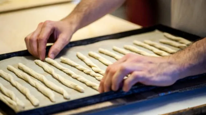 Close-up of incognito male baker hands placing breadsticks dough on baking tray for cooking in oven