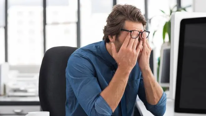 Portrait of an upset businessman at desk in office. Businessman being depressed by working in office. Young stressed business man feeling strain in eyes after working for long hours on computer.