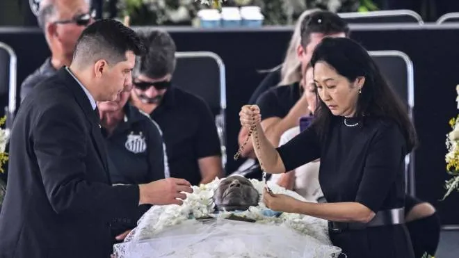 The wife of late Brazilian football legend Pele, Marcia Aoki (R), places a rosary on his coffin during his wake at the Urbano Caldeira stadium in Santos, Sao Paulo, Brazil on January 2, 2023. - Brazilians bid a final farewell this week to football giant Pele, starting Monday with a 24-hour public wake at the stadium of his long-time team, Santos. (Photo by NELSON ALMEIDA / AFP)