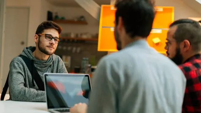Young man at a job interview talking with two developers. They are running startup developer company from their home. Side view of them discussing.