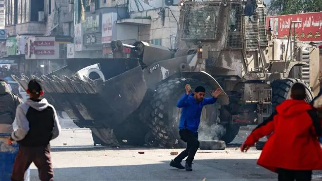 Palestinians hurl rocks at an Israeli army bulldozer, during confrontations in the occupied-West Bank city of Jenin, on January 26, 2023. - An Israeli raid on the West Bank's Jenin refugee camp today killed four Palestinians including an elderly woman, Palestinian officials said, also accusing the army of using tear gas inside a hospital.Israel's army declined to comment when asked by AFP about the health minister's tear gas allegation. (Photo by Zain Jaafar / AFP)