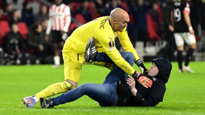 epa10486474 A pitch invader assaults Sevilla FC goalkeeper Marko Dmitrovic during the UEFA Europa league play-off soccer match between PSV Eindhoven and Sevilla FC, in Eindhoven, Netherlands, 23 February 2023.  EPA/OLAF KRAAK