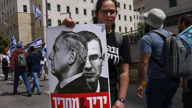 A protester hold up a placard bearing protraits of Israeli Prime Minister Benjamin Netanyahu and behind him Justice Minister Yariv Levin as they gather outside Israel's parliament, the Knesset, in Jerusalem to protest against the hard-right government's controversial push to overhaul the justice system, on March 27, 2023. (Photo by HAZEM BADER / AFP)