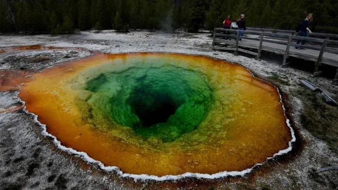 Tourists view the Morning Glory hot spring in the Upper Geyser Basin of Yellowstone National Park in Wyoming, on May 14, 2016. 
The distinctive colors of the hot spring is due to bacteria which survive in the hot water although its vivid color has changed from its original blue to yellow and green after an accumulation of coins and debris thrown by tourists. / AFP PHOTO / Mark Ralston