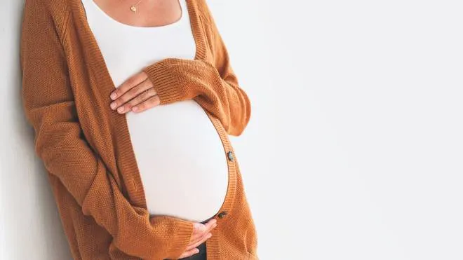 Beautiful pregnant woman touching her belly with hands on a white background. Young mother anticipation of the baby. Image of pregnancy and maternity. Close-up, copy space, indoors. Maternity wear donna in gravidanza incinta