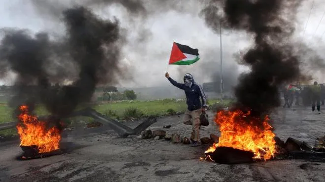 epaselect epa06637253 A Palestinian protester waves Palestine flag during clashes marking Land Day in the West Bank City of Ramallah, 30 March 2018. According to reports, seven Palestinians were killed and more than 500 injured during the clashes along the Gaza border with Israel. Clashes erupted in various locations in the West Bank and alongside the Israeli borders with Gaza as Palestinians hold protests on the occasion of Land Day, the annual day commemorating the events of 30 March 1976 when marches and a general strike was organized in the Arab towns in the occupied lands. The 1976 marches were against the Israeli government announcement to expropriate thousands of acres of land for settlement. It is considered a day for the right of Palestinians to return to their land.  EPA/ALAA BADARNEH