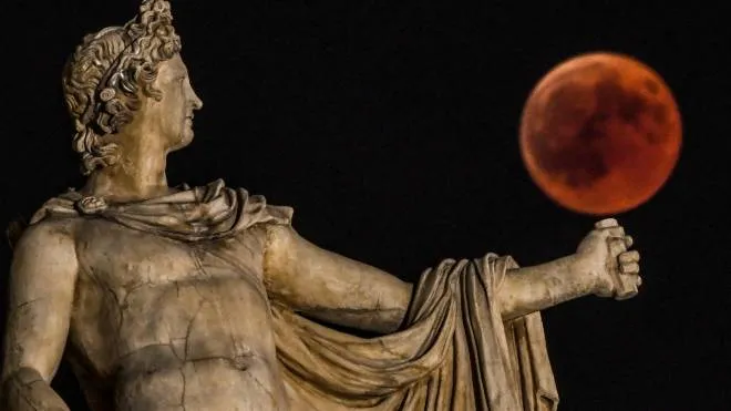 A picture shows the full moon during a &quot;blood moon&quot; eclipse beside a statue of the ancient Greek god Apollo  in central Athens on July 27, 2018.
The longest &quot;blood moon&quot; eclipse this century began on July 27, coinciding with Mars' closest approach in 15 years to treat skygazers across the globe to a thrilling celestial spectacle. / AFP PHOTO / Aris MESSINIS