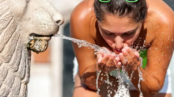 Sweltering hot / Summer heat - Young woman refreshing herself with water from the fountain