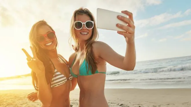 Shot of two friends taking selfies while hanging out at the beach