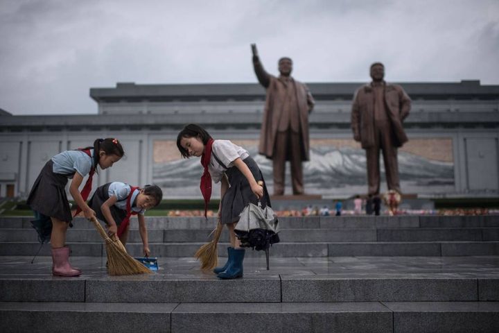 Corea del Nord, giovani studentesse puliscono le scale davanti alle statue dei vecchi leader Kim Il-Sung e Kim Jong-Il durante i festeggiamenti del cosiddetto "Giorno della vittoria", 27 luglio 2017 (Afpm Ed Jones)