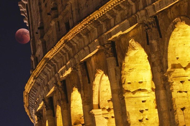 Roma, la Luna rossa sbuca da dietro il Colosseo a Roma (Ansa)